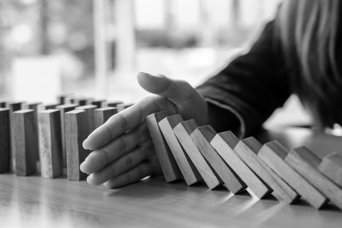 Reihe fallender Dominosteine wird durch eine Hand aufgehalten